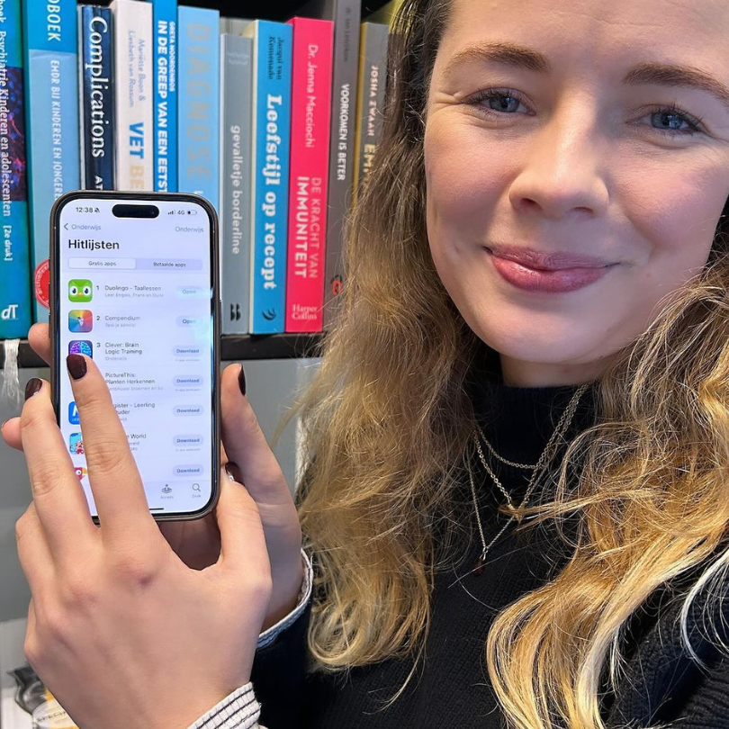 Veerle holding phone showing the Compendium Medicine App in the app store charts