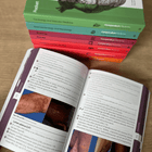 Open Dermatology book with images on different skin colours, with a stack of colourful books in the background.