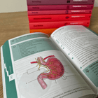 Open book with anatomical diagram of a stomach, stacked books in the background.