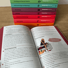 Open First Aid book with colourful stacked books on a wooden surface